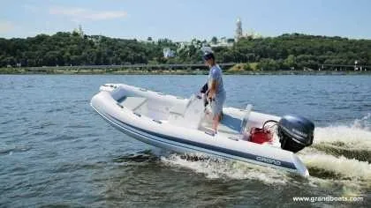 Slide: The Image of 2024 Grand Inflatables S420 boat cruising on a lake with a scenic forest background. - 8