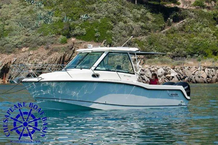 Slide: The Image of 2026 Boston Whaler 285 Conquest boat on calm water near rocky shoreline. - 2