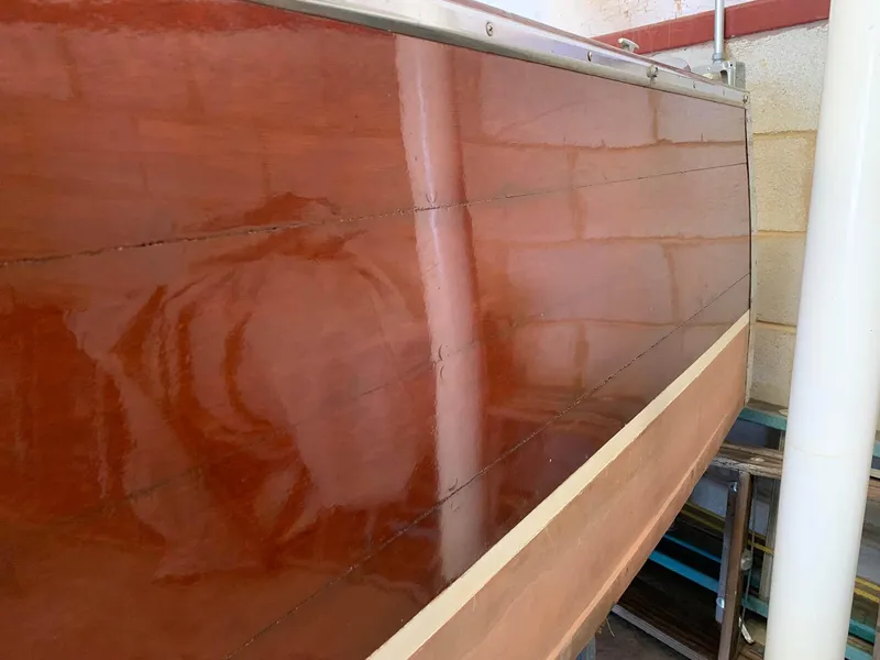 Slide: The Image of 1947 Chris-Craft 17 Runabout Deluxe wooden hull, polished and reflective, in a storage area. - 13