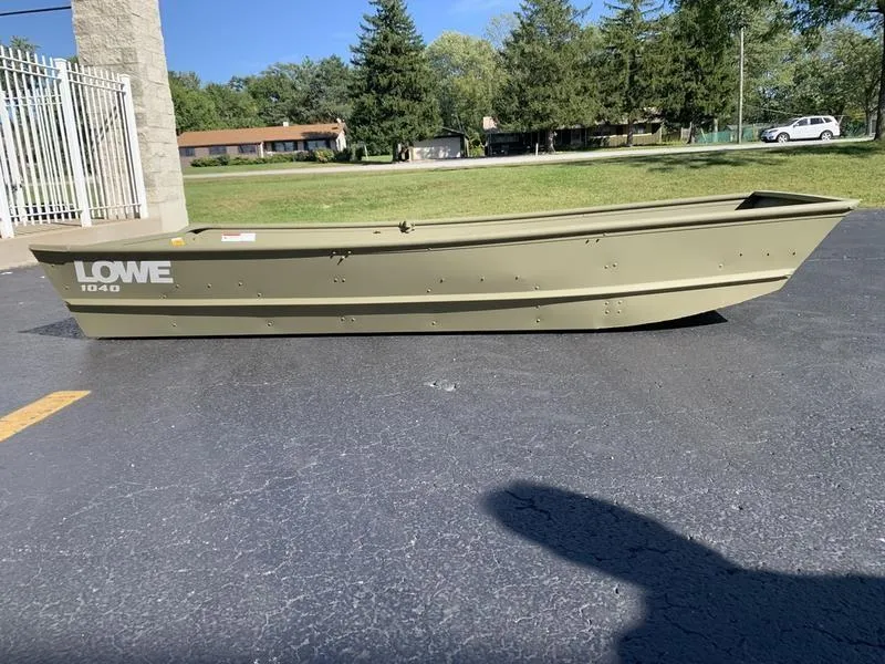 The Image of 2024 Lowe L1040 Jon boat on pavement, surrounded by trees and buildings. - 1