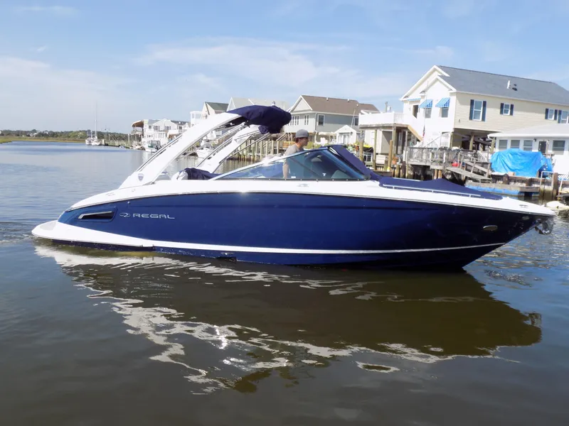 Slide: The Image of 2023 Regal 2800 Bowrider boat on calm water near waterfront homes. - 2