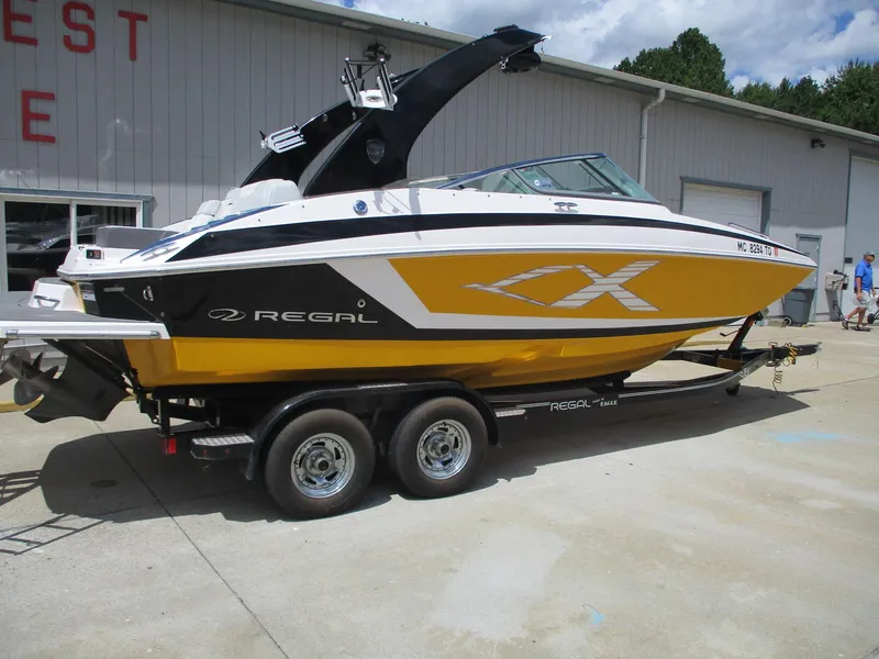 Slide: The Image of 2013 Regal 24 FasDeck RX boat on trailer, yellow and black design, parked outside a building. - 2