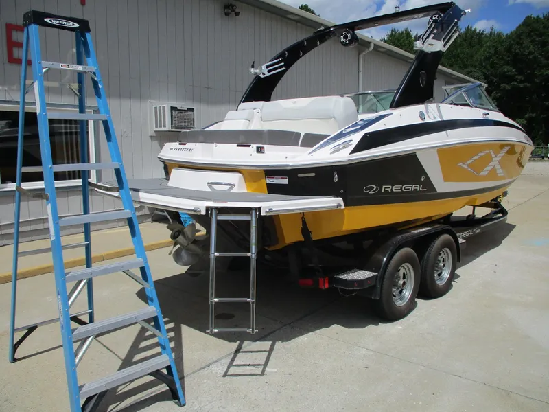 Slide: The Image of 2013 Regal 24 FasDeck RX boat on trailer, yellow and black design, parked near a building. - 3