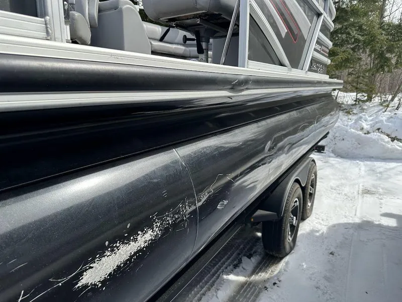 Slide: The Image of 2021 Ranger 243C boat with visible side damage and scratches in a snowy environment. - 6