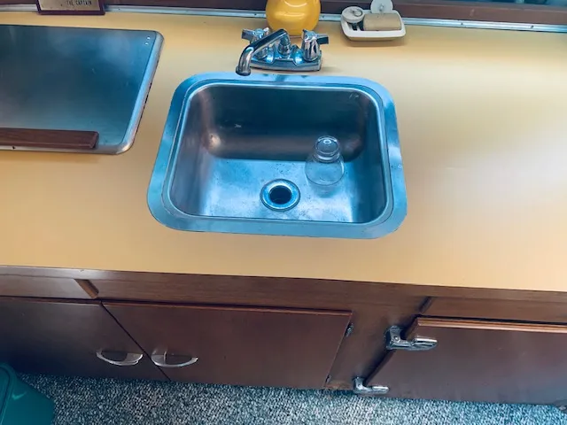 Slide: The Image of 1969 Chris-Craft Commander Sedan kitchen sink with yellow countertop and wooden cabinets. - 16