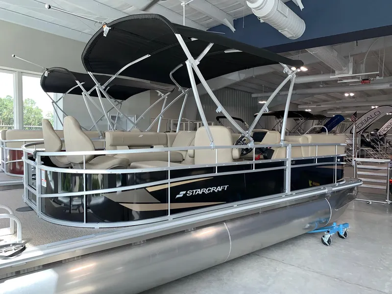 Slide: The Image of 2024 Starcraft LX20 F pontoon boat with black canopy in showroom. - 1