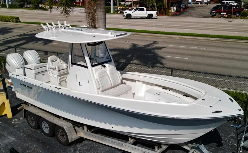 Slide: The Image of 2023 Regulator 28 boat on trailer, white exterior, dual engines, parked near a road. - 23