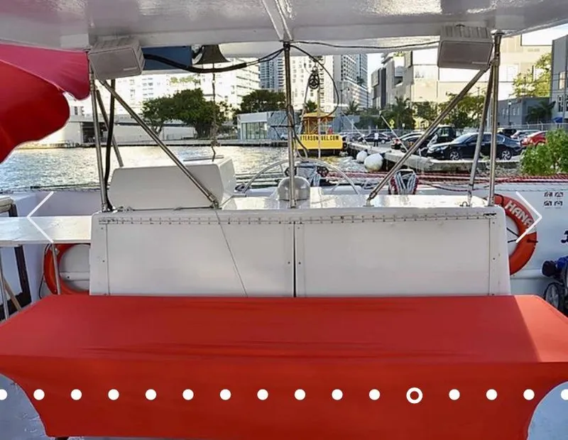 Slide: The Image of 1987 Custom Suncoast Catamaran with red seating, docked near waterfront buildings. - 2