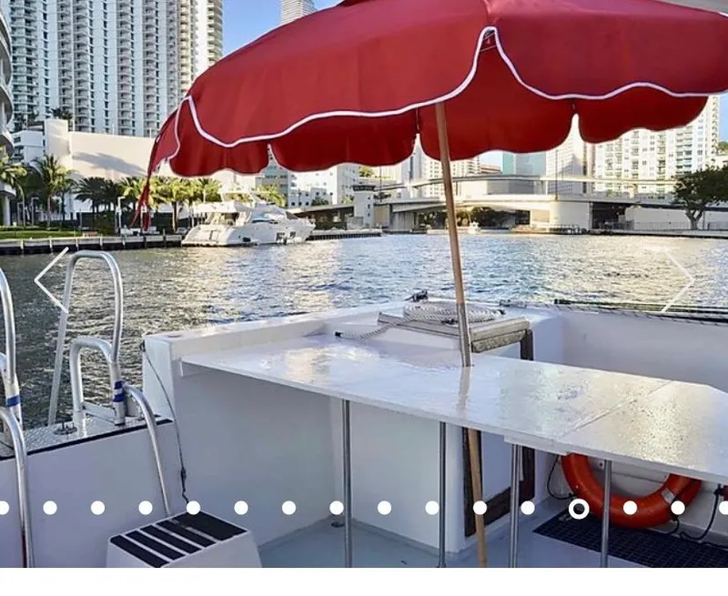 Slide: The Image of 1987 Custom Suncoast Catamaran with red umbrella, docked near city waterfront. - 3