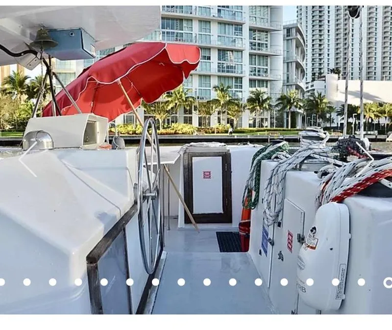 Slide: The Image of 1987 Custom Suncoast Catamaran deck with red canopy, docked near modern buildings. - 4
