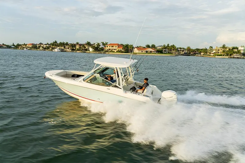 Slide: The Image of 2023 Boston Whaler 240 Vantage cruising on water near coastal homes. - 42