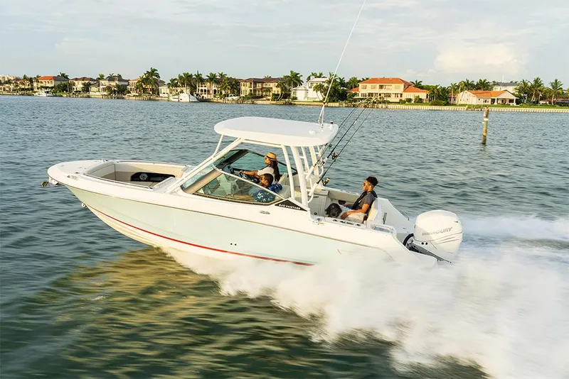 Slide: The Image of 2023 Boston Whaler 240 Vantage cruising on water near coastal homes. - 8
