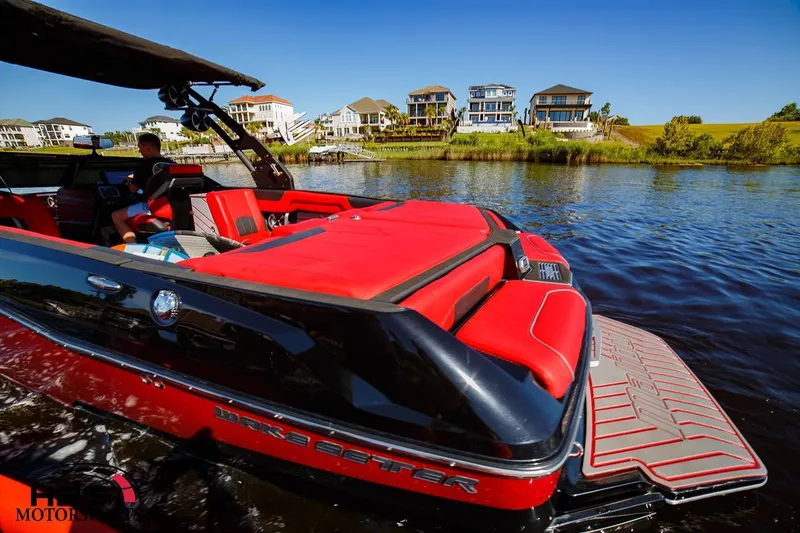 Slide: The Image of 2019 Malibu Wakesetter 25 LSV boat with red interior on a lake near luxury homes. - 5