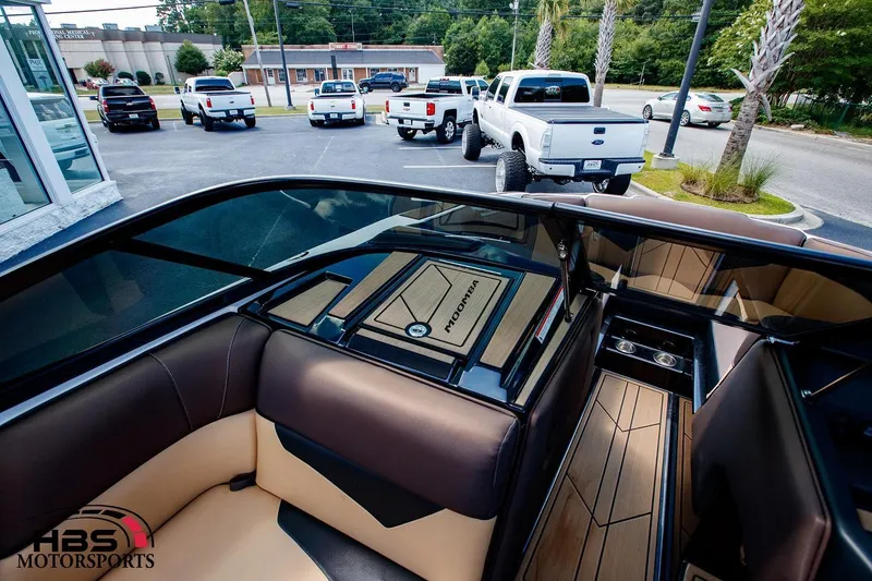 Slide: The Image of 2020 Moomba Kaiyen boat interior with tan and black seating, parked trucks in background. - 8