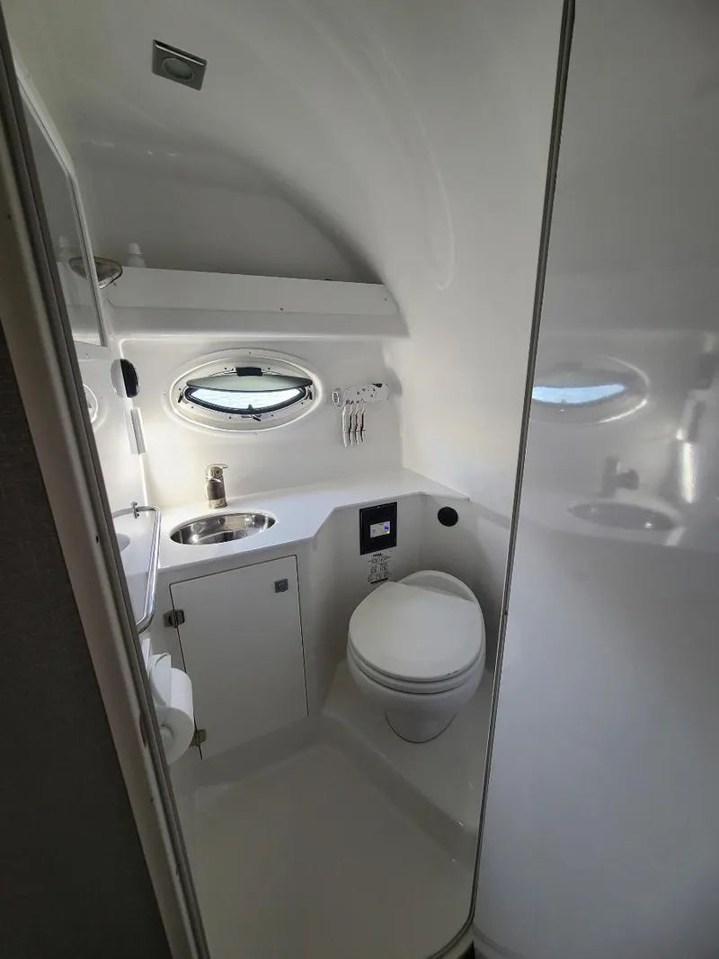 Slide: The Image of 2018 Monterey 295 Sport Yacht bathroom with sink, toilet, and porthole window. - 11