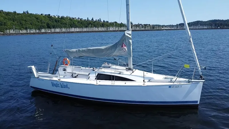 Slide: The Image of 2015 Catalina 275 Sport sailboat on calm water, with lush green shoreline in the background. - 11