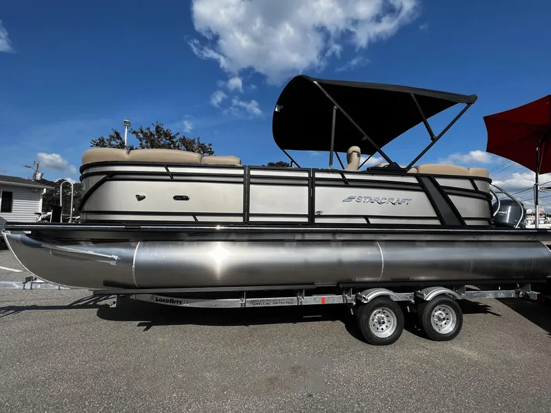 The Image of 2024 Starcraft SLS 3 pontoon boat on a trailer under a blue sky. - 0