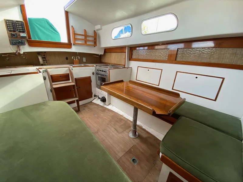 Slide: The Image of 1968 Pearson Wanderer sailboat interior with green cushions, wooden table, and compact kitchen area. - 25