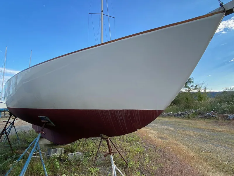 Slide: The Image of 1968 Pearson Wanderer sailboat on land, white hull with red bottom, clear sky background. - 7