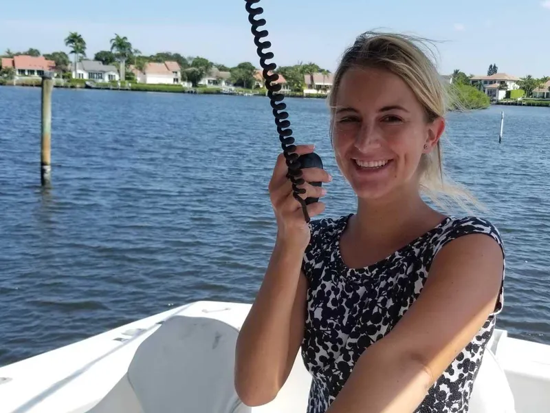Slide: The Image of A woman smiling on a boat, holding a radio, with waterfront homes in the background. - 4