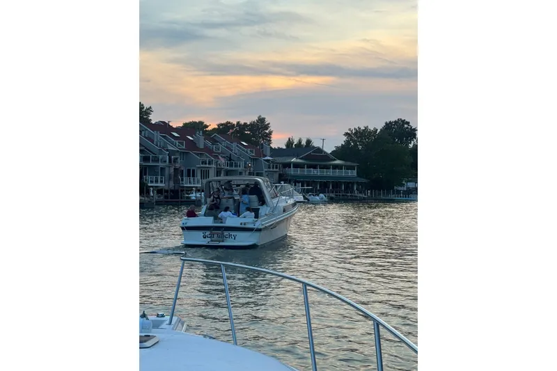 Slide: The Image of 1988 Carver 32 Montego boat cruising on a serene lake at sunset, near waterfront homes. - 22