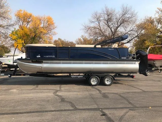Slide: The Image of 2023 Harris Cruiser 230 pontoon boat on trailer, parked outdoors in autumn setting. - 10