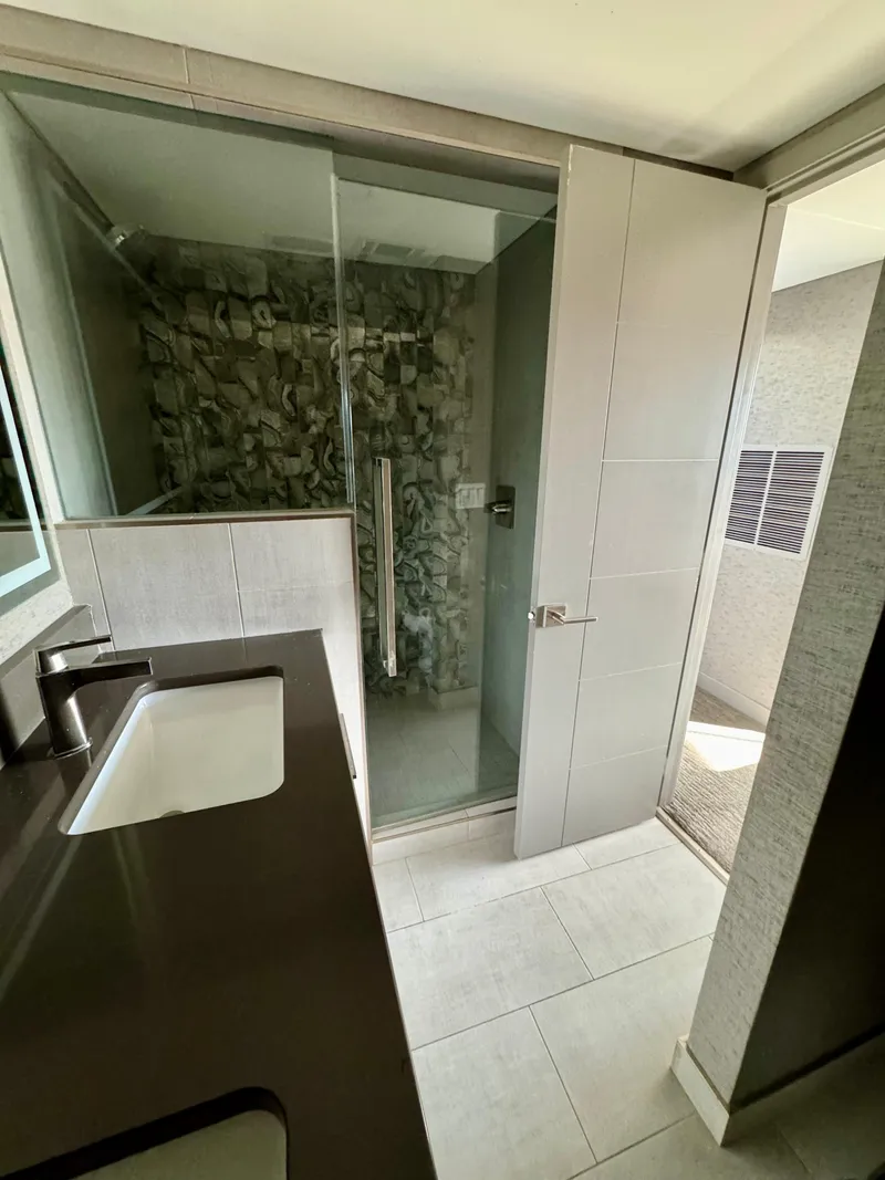 Slide: The Image of Modern bathroom with glass shower, stone wall, and sleek dark countertop. Adonia Just Add Water Trip #13, 2021. - 22