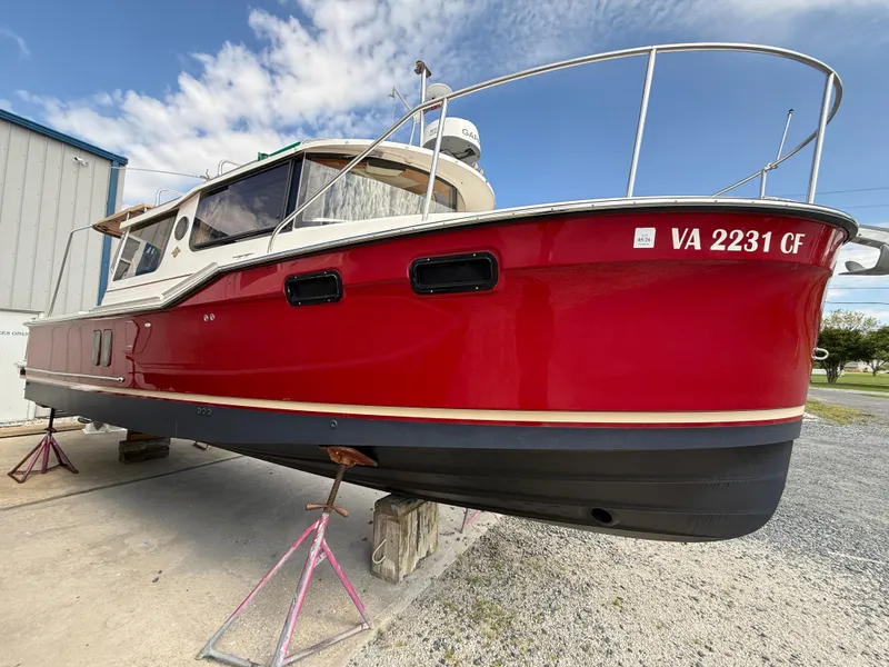 Slide: The Image of 2020 Ranger Tugs R-27 boat in vibrant red, docked on land under a clear sky. - 2