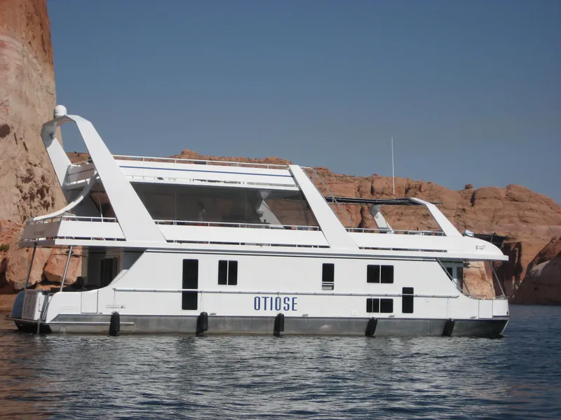 Slide: The Image of Custom 2005 houseboat The Entourage Shares 20 & 35 on a serene lake with rocky backdrop. - 2