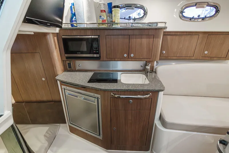 Slide: The Image of 2019 Boston Whaler 315 Conquest cabin kitchen with microwave, sink, and wooden cabinetry. - 111