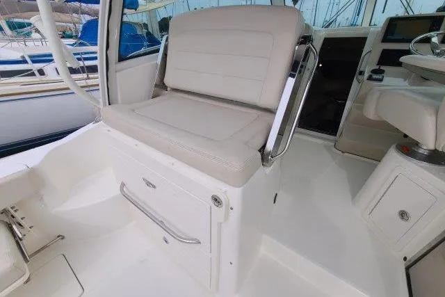 Slide: The Image of 2019 Boston Whaler 315 Conquest interior seating with white upholstery and storage compartment. - 19