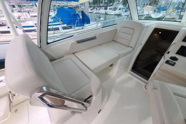 Slide: The Image of 2019 Boston Whaler 315 Conquest interior seating area with white upholstery and marina view. - 22