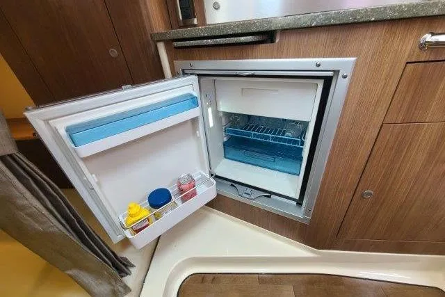 Slide: The Image of Compact refrigerator inside 2019 Boston Whaler 315 Conquest boat, featuring wooden cabinetry and open door. - 70