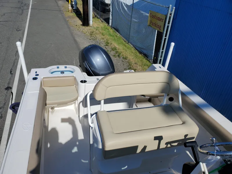 Slide: The Image of 2022 Sailfish 220 WAC boat interior with seating and motor, parked near a blue building. - 8