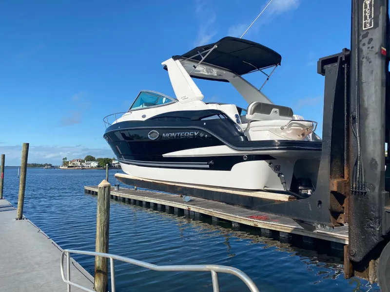 Slide: The Image of 2015 Monterey 275 Sport Yacht on a boat lift by the water. - 47