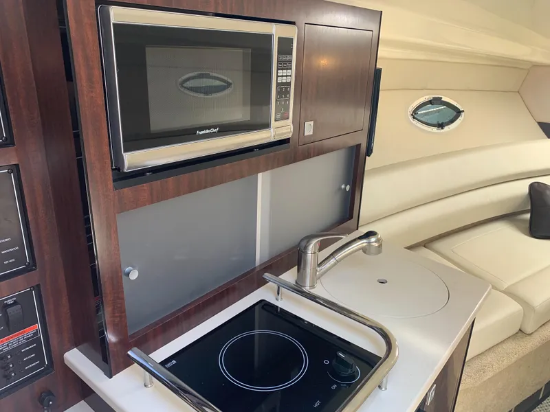 Slide: The Image of Interior view of a 2015 Monterey 275 Sport Yacht featuring a compact kitchen with microwave and stove. - 12