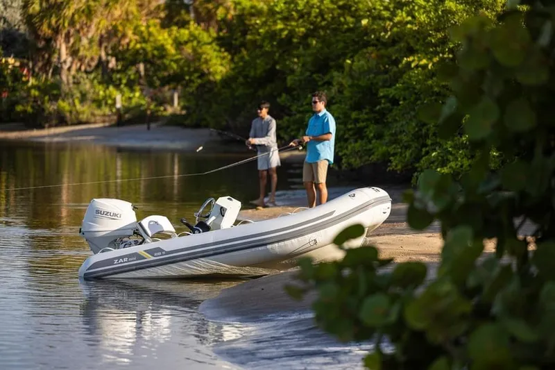 Slide: The Image of Two people fishing near a 2022 ZAR Mini Rib HDL10 boat on a sandy shore. - 12