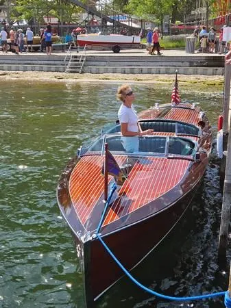 Slide: The Image of 1989 Hacker-Craft Triple Cockpit boat docked, with a person onboard, near a lively waterfront. - 23