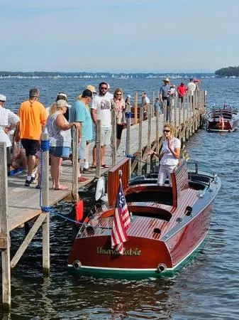 Slide: The Image of 1989 Hacker-Craft Triple Cockpit boat docked with people on pier, American flag displayed. - 26