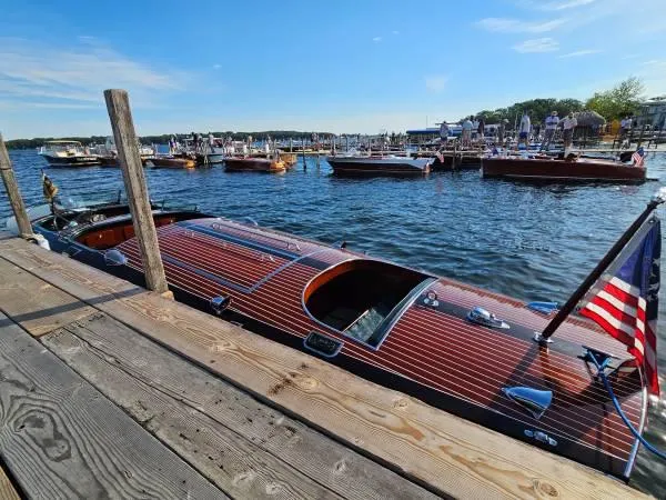 Slide: The Image of 1989 Hacker-Craft Triple Cockpit boat docked by a wooden pier, with other boats in the background. - 27