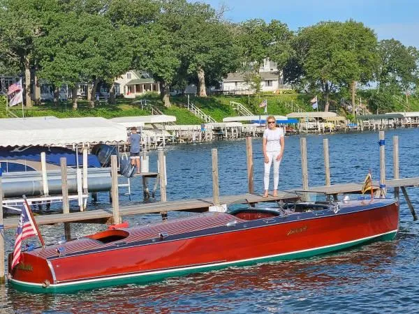 Slide: The Image of 1989 Hacker-Craft Triple Cockpit boat docked by a lakeside with a person standing nearby. - 29