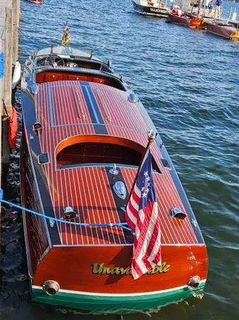 Slide: The Image of 1989 Hacker-Craft Triple Cockpit boat docked, featuring polished wood and American flag. - 32