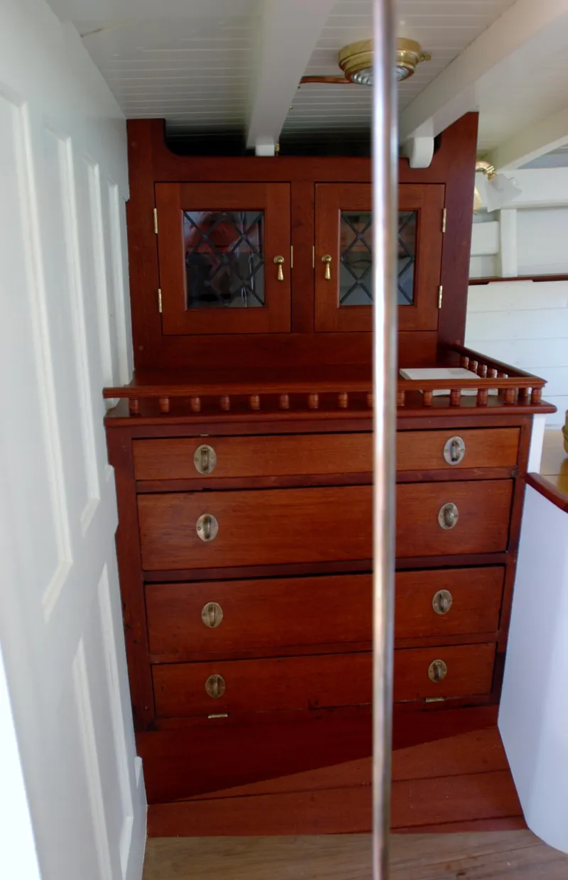 Slide: The Image of Antique wooden cabinetry inside 1902 Herreshoff Gaff Cutter yacht, featuring drawers and glass-paneled doors. - 21