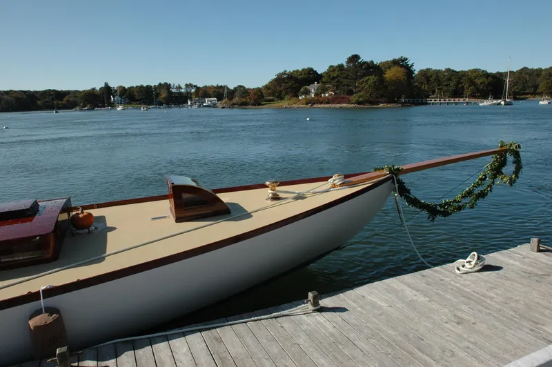 Slide: The Image of A 1902 Herreshoff Gaff Cutter docked by a serene lake with lush greenery. - 6