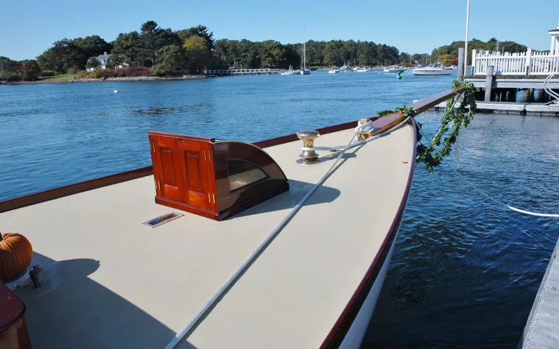 Slide: The Image of Herreshoff Gaff Cutter 1902 docked on a serene waterfront with lush greenery. - 7