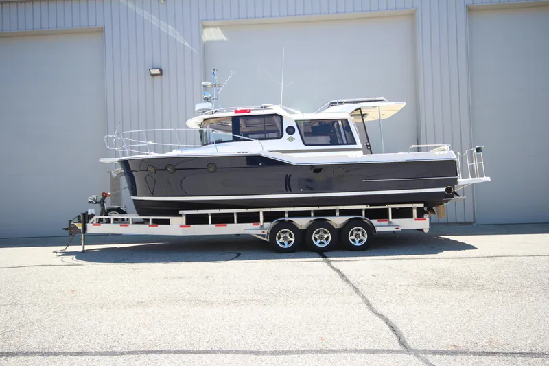 The Image of 2026 Ranger Tugs R-29 S boat on a trailer, parked outside a large garage. - 0