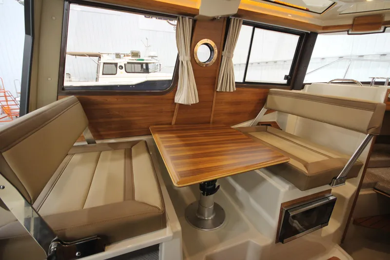 Slide: The Image of 2025 Ranger Tugs R-23 interior dining area with wood table and cushioned seating. - 26