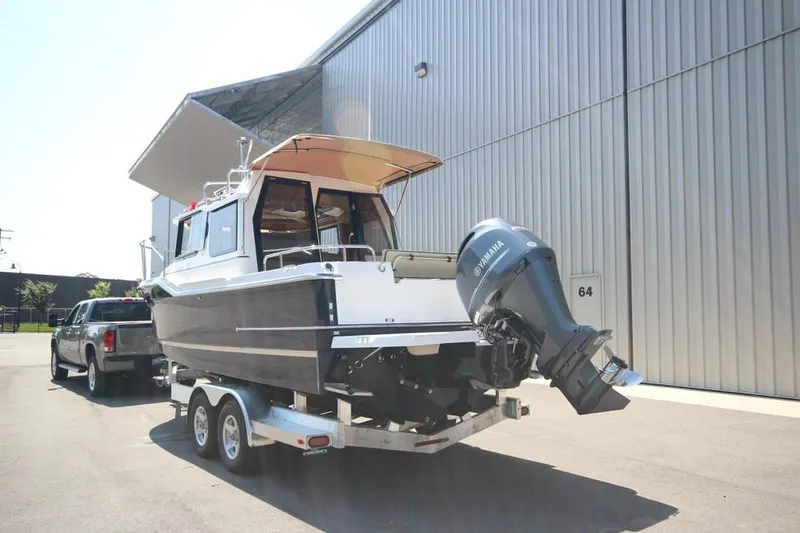 Slide: The Image of 2025 Ranger Tugs R-23 boat on trailer, parked outside a large metal building. - 3