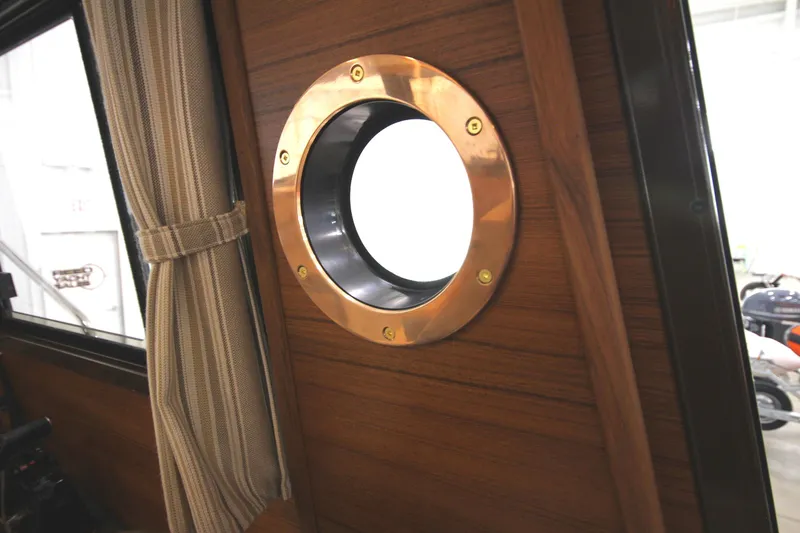 Slide: The Image of 2025 Ranger Tugs R-23 interior porthole with wooden paneling and curtain. - 30