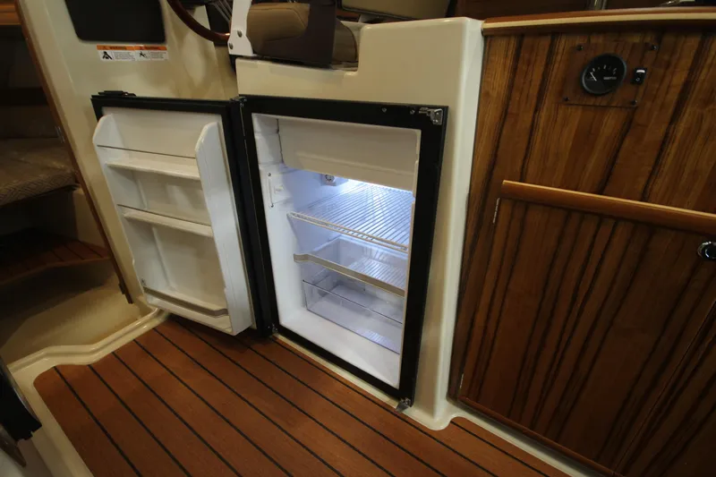 Slide: The Image of 2025 Ranger Tugs R-23 boat interior with open refrigerator and wooden cabinetry. - 31
